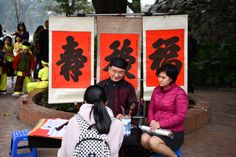 three people are sitting at a table in front of two red and white banners with chinese characters on them