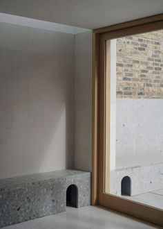 an empty room with a large window and stone bench in front of the window, next to a brick wall