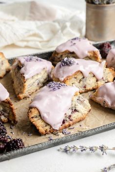 a tray filled with muffins covered in frosting next to some blackberries