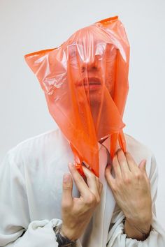 a man with an orange plastic bag on his head is holding something in front of his face