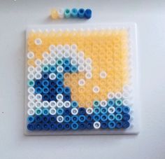 a piece of art made out of legos on a white surface with blue and yellow beads