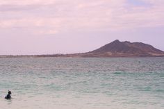 two people swimming in the ocean with a mountain in the backgroung area