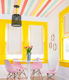 a dining room with yellow walls and colorful striped ceilinging, pink chairs and a white round table