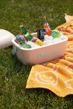 a pink cooler filled with drinks sitting on top of a green grass covered field next to an orange towel