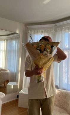 a man holding flowers in his hands while standing in front of a window with curtains