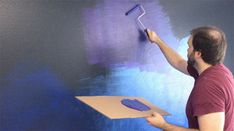 a man painting a wall with purple paint and a blue roller on the wall next to it