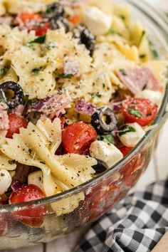 a pasta salad with tomatoes, olives, and other vegetables in a glass bowl