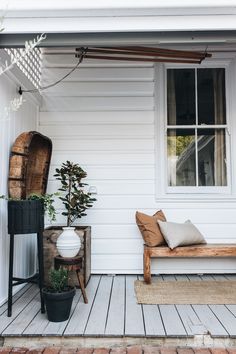 a porch with a bench, planter and potted plants on the side of it