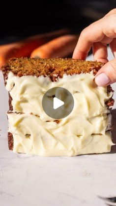 a person holding a piece of cake with cream cheese frosting on it and the video is in front of them