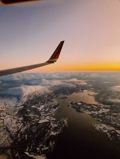 the wing of an airplane as it flies over snow covered mountains and lakes at sunset