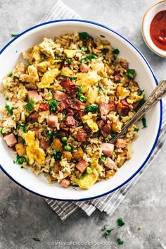 a bowl filled with rice, ham and peas on top of a cloth next to a spoon