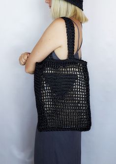 a woman with blonde hair is carrying a black crocheted tote bag on her back