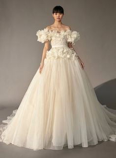 a woman in a wedding dress with flowers on the shoulders and shoulder, standing against a gray background