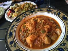 a plate with some food on it next to a bowl of salad and a glass of wine