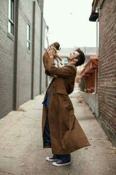 a man holding a small dog in his right hand and looking up at the sky