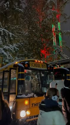 a school bus driving down a snowy street with christmas lights on the trees behind it