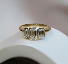 three stone diamond ring sitting on top of a white object with gold trimmings