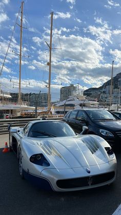 two sports cars parked next to each other in front of a sailboat docked at a marina