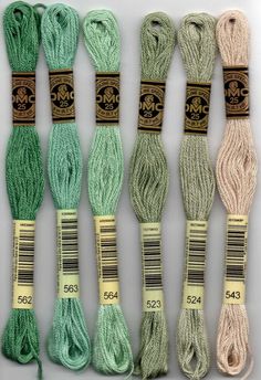 six skeins of green, white and beige colored yarn are lined up in rows