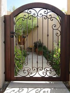 an iron gate in front of a house with potted plants on the side walk