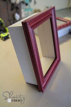 a red frame sitting on top of a table next to a white box with a mirror in it