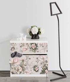 a white and pink flowered dresser with two drawers next to a black floor lamp