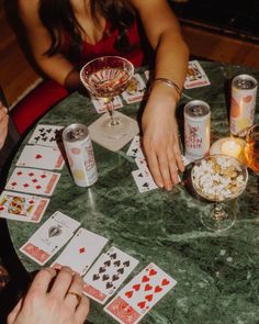 two people playing cards at a table with drinks and snacks on it, while another person holds their hand