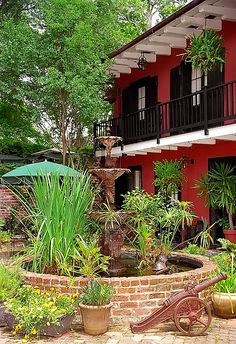 a red house with an umbrella and water fountain in the front yard, surrounded by potted plants