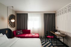 a hotel room with a bed, desk and red chair in front of a large window