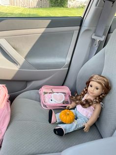 a doll sitting in the back seat of a car next to a pink backpack and pumpkin