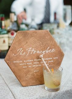 a wooden sign sitting on top of a table next to a glass filled with liquid