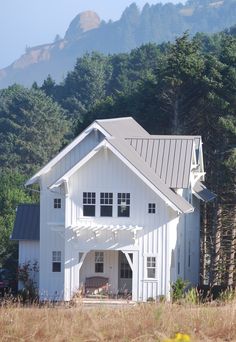 a white house sitting in the middle of a field next to tall grass and trees