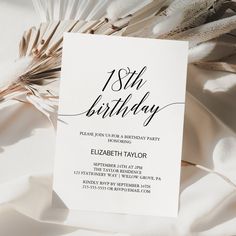 a white birthday party card with black lettering on it and feathers in the foreground