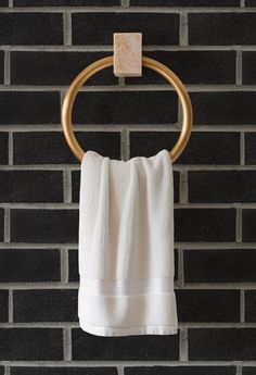 a white towel hanging on a gold ring in front of a brick wall