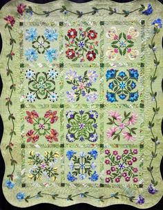 a green quilt with flowers and leaves on the front, along with an embroidered border