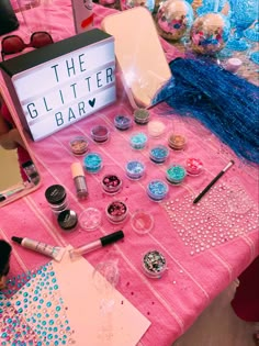 the glitter bar is set up on a pink tablecloth with various items