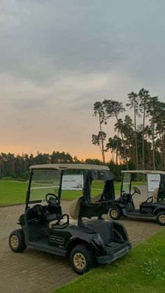 two golf carts parked on the side of a dirt road next to a green field