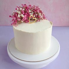 a white cake with pink and white flowers on top is sitting on a plate in front of a pink wall