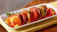 a white plate topped with sliced vegetables on top of a wooden table next to a yellow napkin