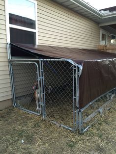 a dog is in its kennel on the side of a house with a tarp over it