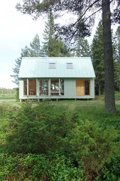 a small green house in the middle of some trees and bushes with a blue roof