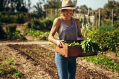 a woman holding a crate full of vegetables in her hands and smiling at the camera