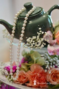 a green teapot with pearls and flowers in it sitting on a cake platter