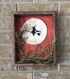 a red and white plaque with a witch on it in a wooden frame hanging on a brick wall