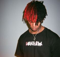 a young man with red dreadlocks looking down at his cell phone while wearing a black shirt