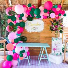 a table topped with lots of balloons next to a wall covered in pink and green