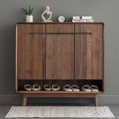 a wooden cabinet sitting on top of a rug next to a white vase and potted plant