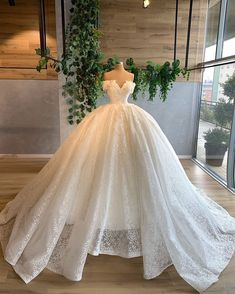 a white wedding dress on display in front of a window with greenery hanging from it