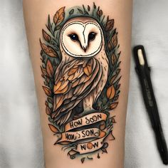 an owl tattoo on the leg with words below it and leaves around it, as well as a banner