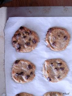 six chocolate chip cookies sitting on top of a white paper lined baking sheet, ready to be baked